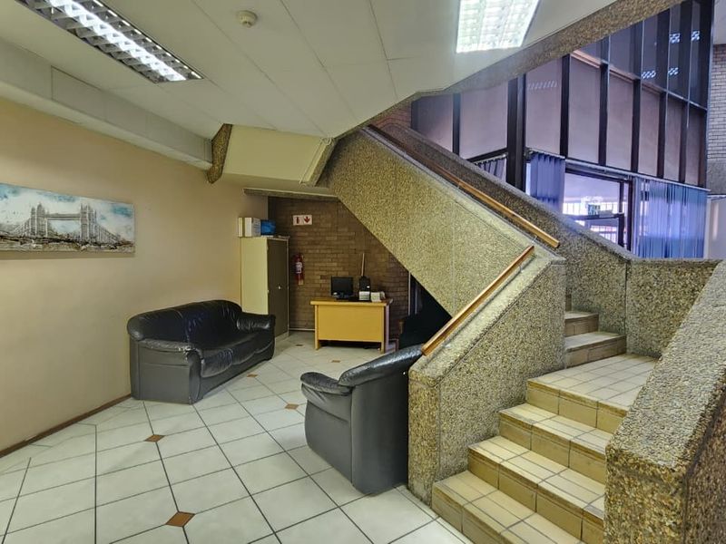 Spacious office building entrance featuring a prominent exposed aggregate concrete staircase, tiled flooring, and a brick feature wall.