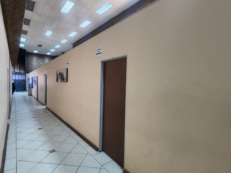 A long office hallway featuring tiled flooring, suspended ceilings with recessed lighting, and multiple access doors to individual office spaces.