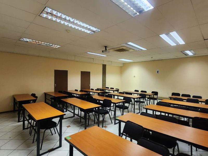 A functional office or training room featuring suspended ceilings with recessed lighting, tiled flooring, and a central air conditioning unit.