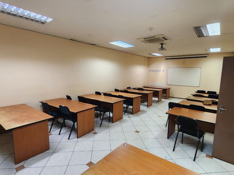 A functional office or training room featuring tiled flooring, recessed ceiling lights, integrated air conditioning, and a wall-mounted whiteboard.