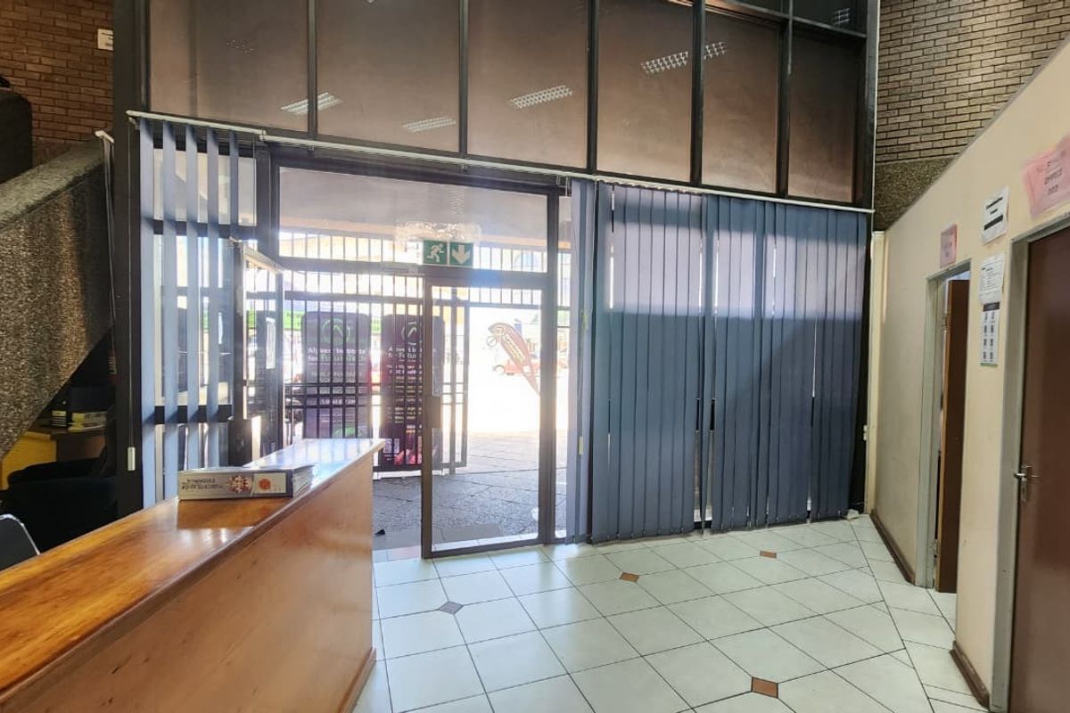 Office building entrance lobby featuring a built-in reception desk, tiled flooring, and large glass storefront windows with vertical blinds.
