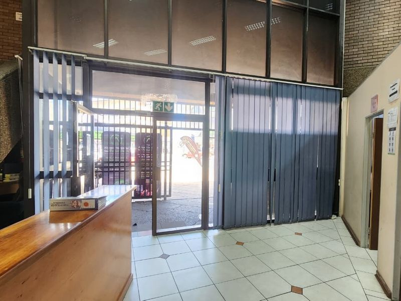 Office building entrance lobby featuring a built-in reception desk, tiled flooring, and large glass storefront windows with vertical blinds.