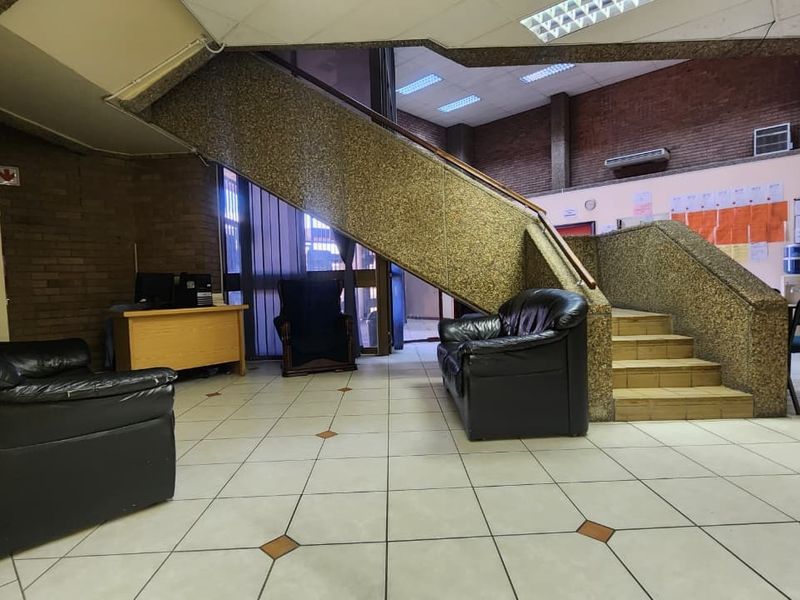 Spacious office entrance area featuring a central staircase, tiled flooring, and exposed brick walls, offering a functional reception or waiting space.