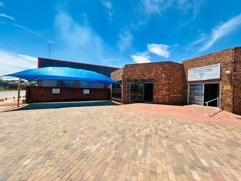 Front exterior view of a commercial medical practice featuring a brick facade, paved parking area, and a blue shade sail structure.