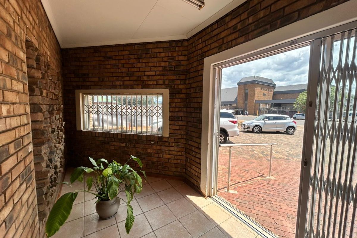 Entrance area featuring exposed brick walls, ceramic tile flooring, and a security gate leading to an outdoor paved parking area.