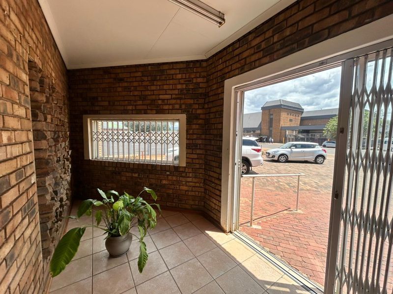 Entrance area featuring exposed brick walls, ceramic tile flooring, and a security gate leading to an outdoor paved parking area.