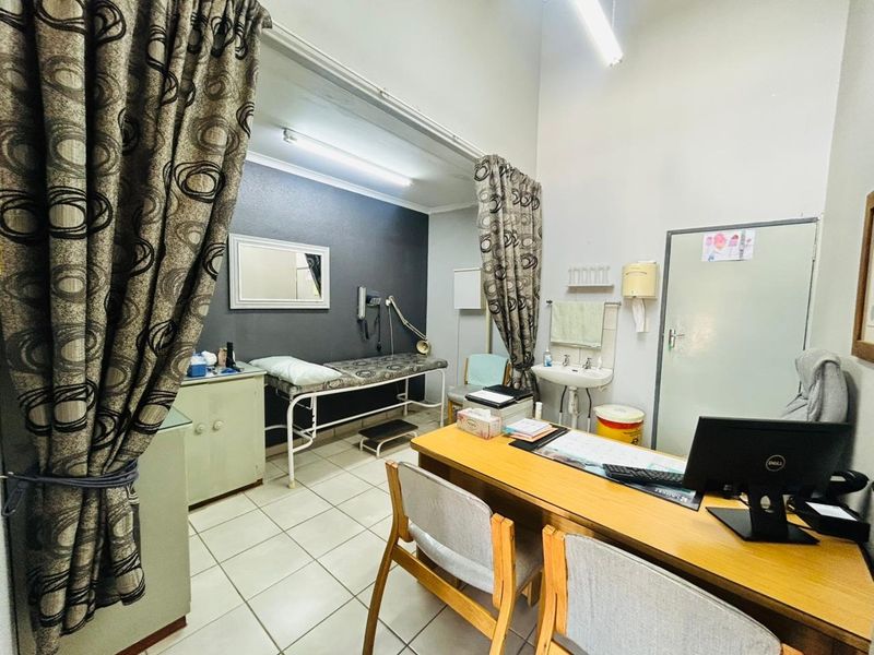 A functional medical or utility consultation room featuring tiled flooring, a wall-mounted basin, and built-in cabinetry, suitable for professional or clinical use.