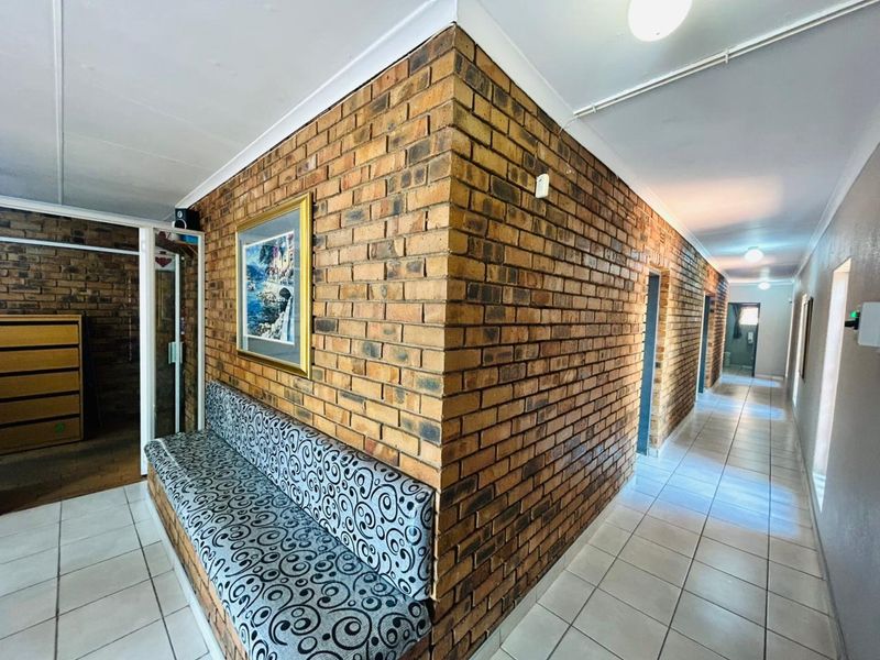 A commercial hallway featuring exposed brick walls, ceramic tiled flooring, and recessed lighting, providing access to multiple rooms.
