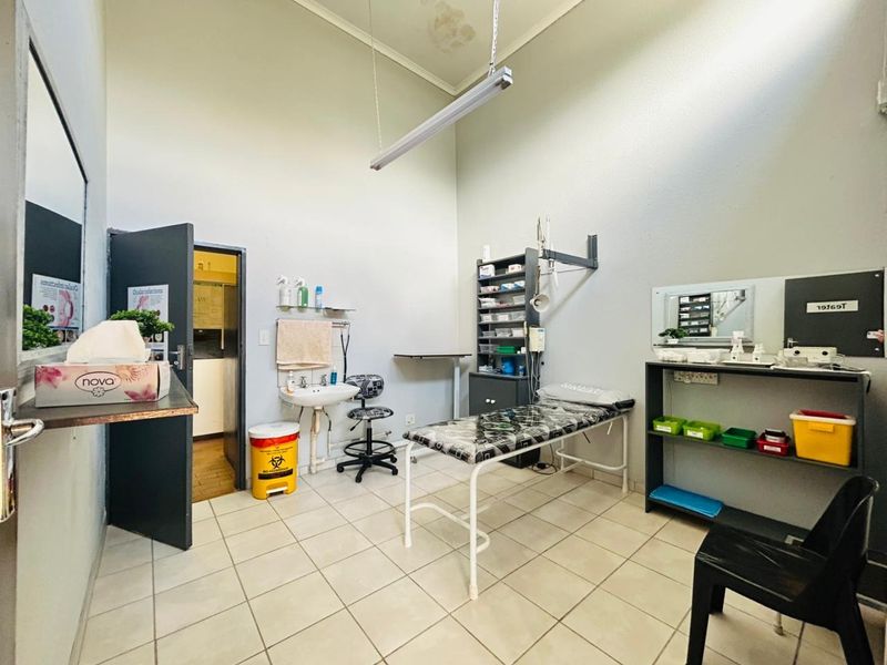 A functional clinical utility room featuring ceramic floor tiles, a wall-mounted basin, and built-in storage shelving, suitable for medical or professional use.