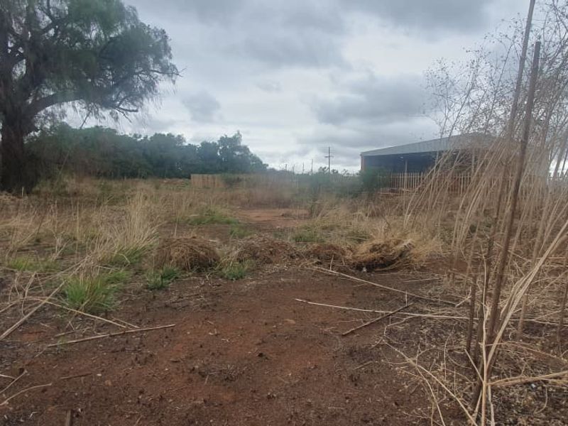 A view of the rear portion of the vacant commercial land, featuring natural terrain, mature trees, and perimeter fencing.