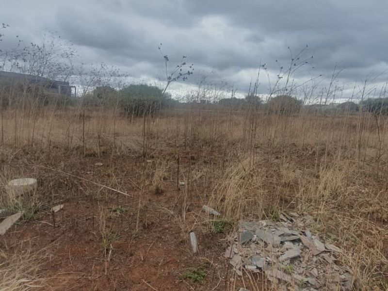 An undeveloped commercial land plot featuring overgrown dry vegetation and scattered debris, suitable for future development.