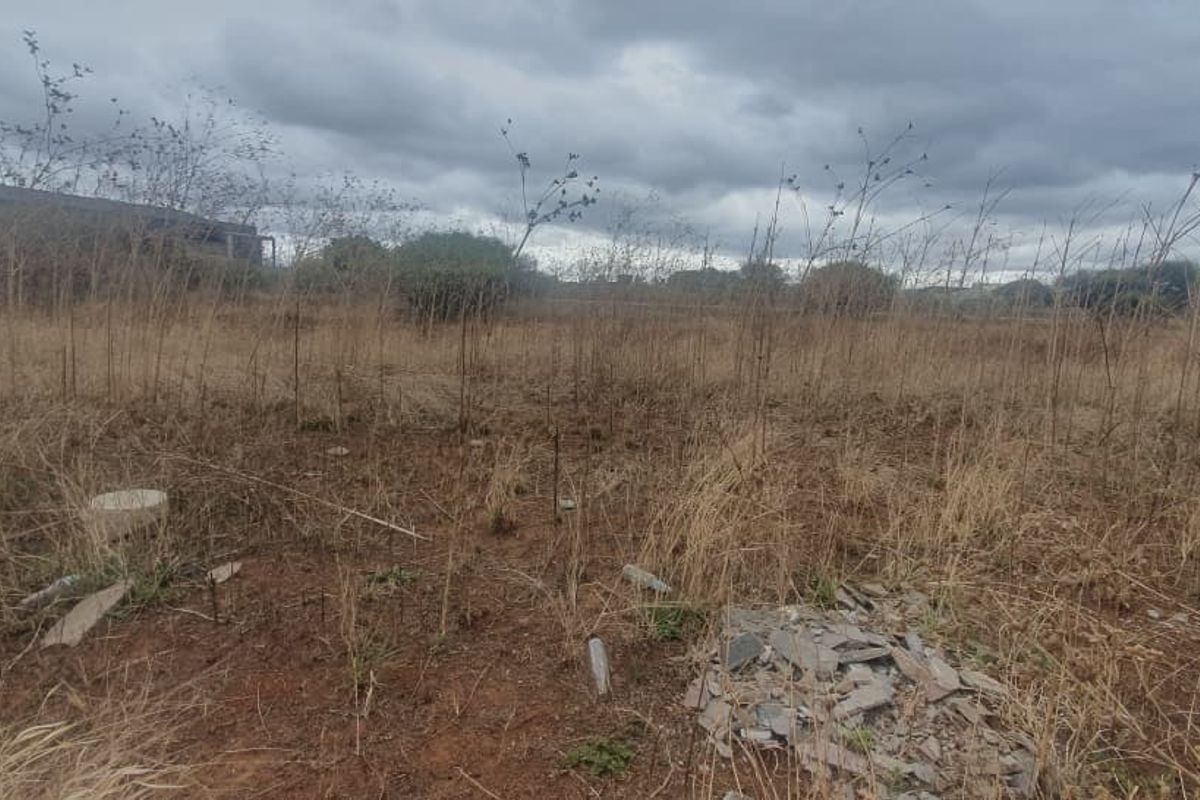An undeveloped commercial land plot featuring overgrown dry vegetation and scattered debris, suitable for future development.