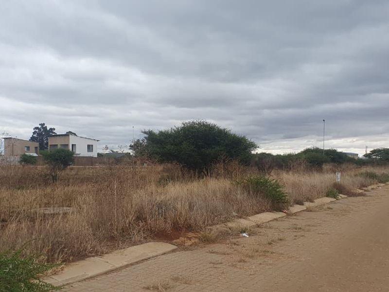 A street-level view of a vacant commercial land plot featuring paved road access, kerbing, and existing street lighting infrastructure.