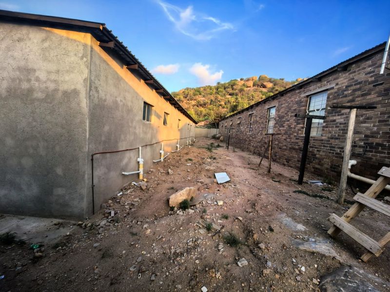 Rear exterior view showing the space between two apartment buildings with exposed plumbing and unfinished ground surface requiring landscaping.