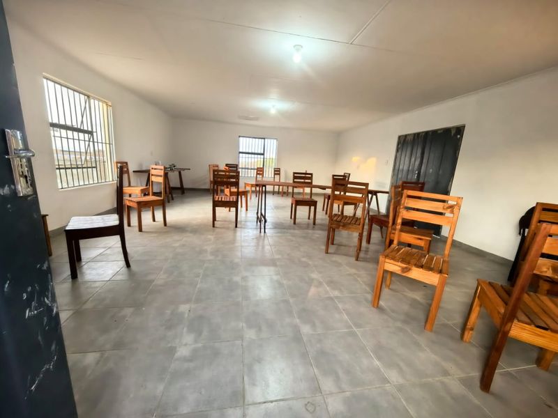 A spacious, open-plan living area featuring tiled flooring and security bars on the windows, offering a blank canvas for potential interior design updates.