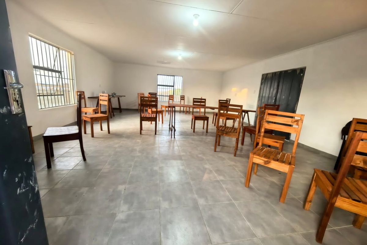 A spacious, open-plan living area featuring tiled flooring and security bars on the windows, offering a blank canvas for potential interior design updates.