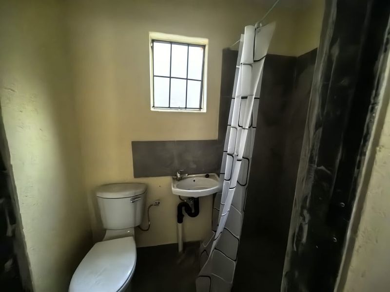 A compact bathroom featuring a toilet, wall-mounted basin, and shower area, currently requiring cosmetic updates and finishing to the wall surfaces.