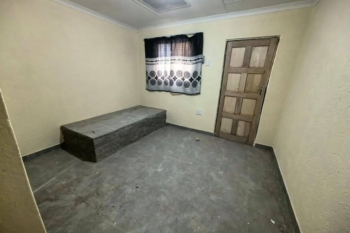 A basic, empty bedroom featuring tiled flooring, a built-in brick platform, and a wooden door, offering a blank canvas for renovation.
