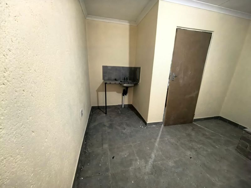 A small, basic kitchen area featuring a single sink, tiled splashback, and tiled flooring, currently in need of cosmetic updates and maintenance.