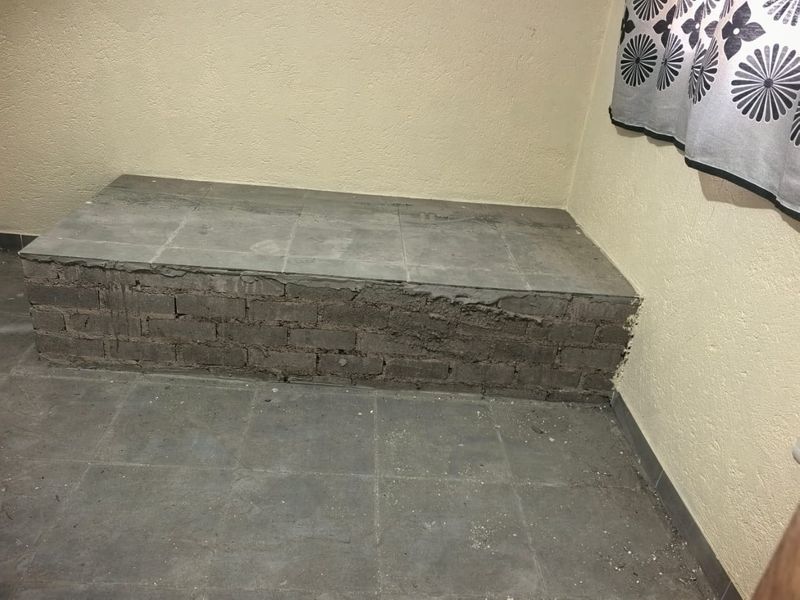 An unfinished tiled platform structure with exposed brickwork, requiring finishing or removal to improve the aesthetic and functional quality of the space.