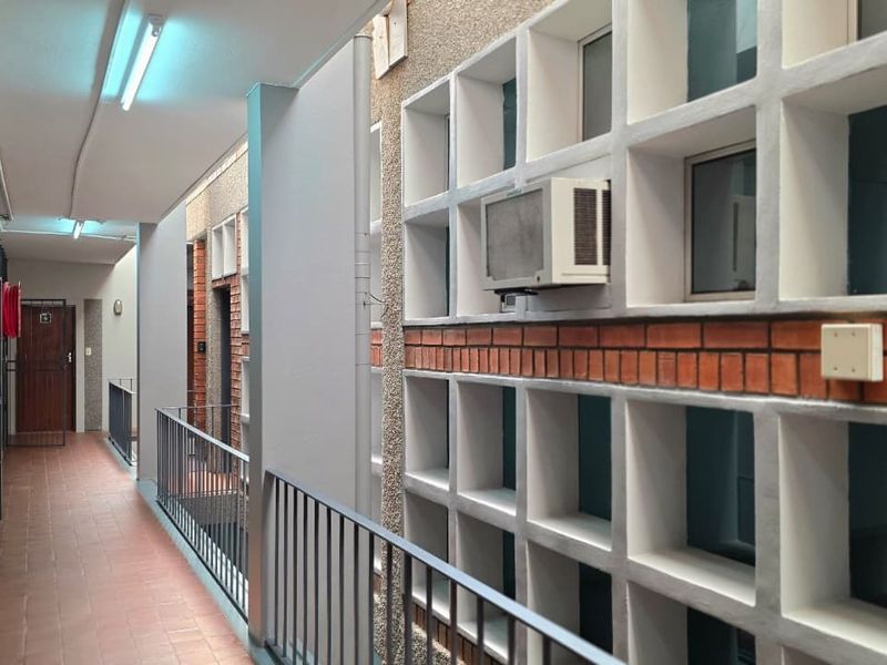 An exterior office building corridor featuring tiled flooring, metal balustrades, and a brick-accented facade with integrated window air conditioning units.