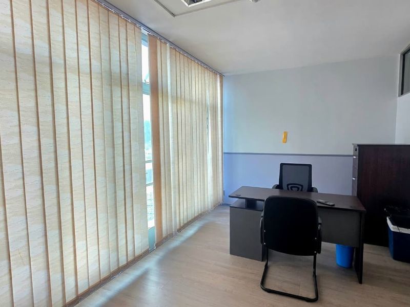 A functional office space featuring laminate flooring, a dado rail, and large windows fitted with vertical blinds for natural light control.