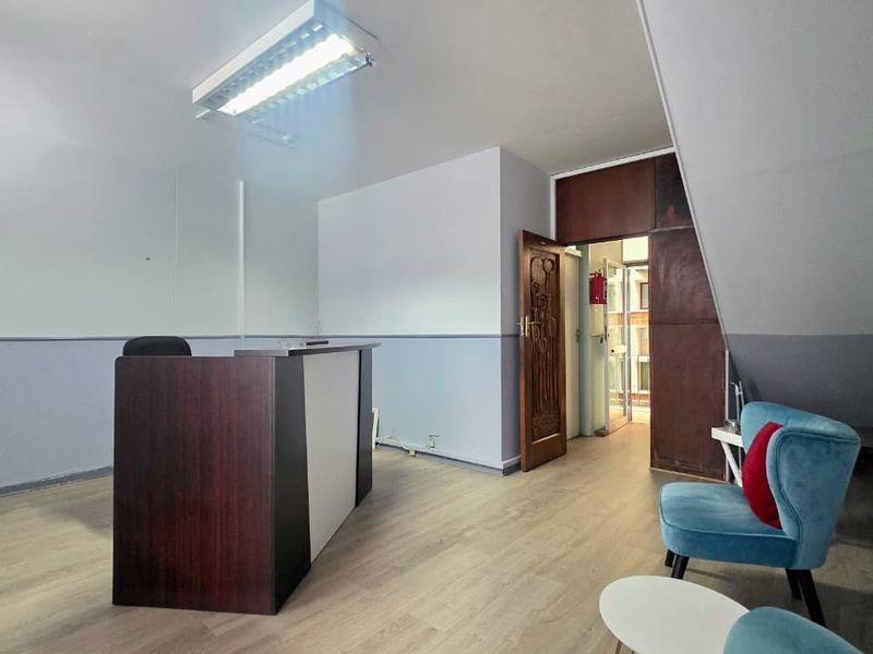 A functional office reception area featuring laminate flooring, a built-in desk, and overhead fluorescent lighting.