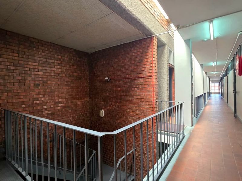 A functional office building hallway featuring exposed brick walls, tiled flooring, and a metal balustrade overlooking the stairwell.
