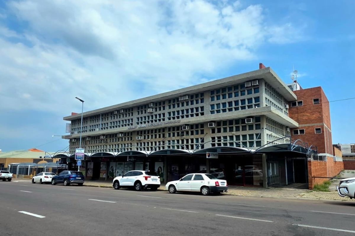 Street-level view of a multi-story commercial office building featuring a distinctive concrete grid facade and a covered ground-floor retail or office entrance area.
