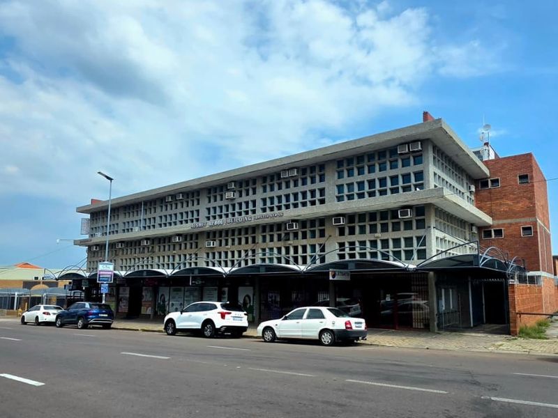 Street-level view of a multi-story commercial office building featuring a distinctive concrete grid facade and a covered ground-floor retail or office entrance area.