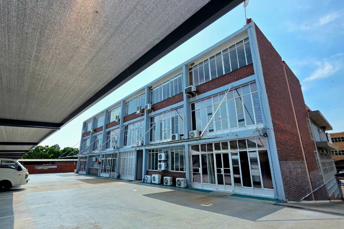 Rear exterior view of a multi-story office building featuring brick facade, extensive glazing, and a covered parking area.