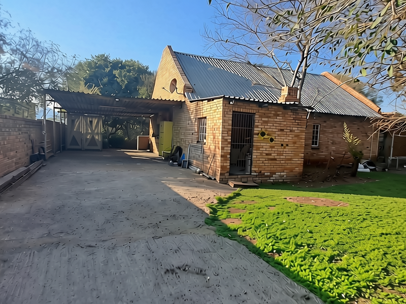 Rear view of a face brick commercial property featuring a concrete driveway, attached carport, and established garden area.