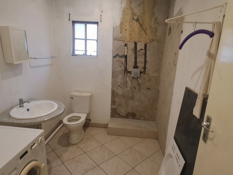 A bathroom in need of renovation, featuring a toilet, washbasin, and shower area with damaged wall finishes and exposed plumbing.