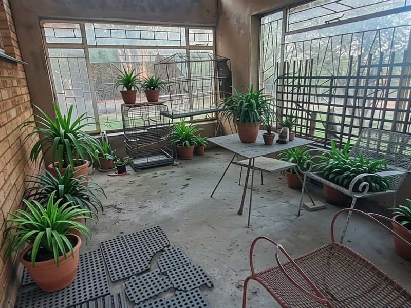 A covered patio area featuring exposed brick walls, large steel-framed windows, and concrete flooring, offering a versatile space for outdoor relaxation.
