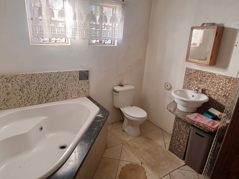 A functional bathroom featuring a corner bathtub, pedestal washbasin, and toilet with tiled splashbacks and flooring, requiring cosmetic updates to modernize the space.
