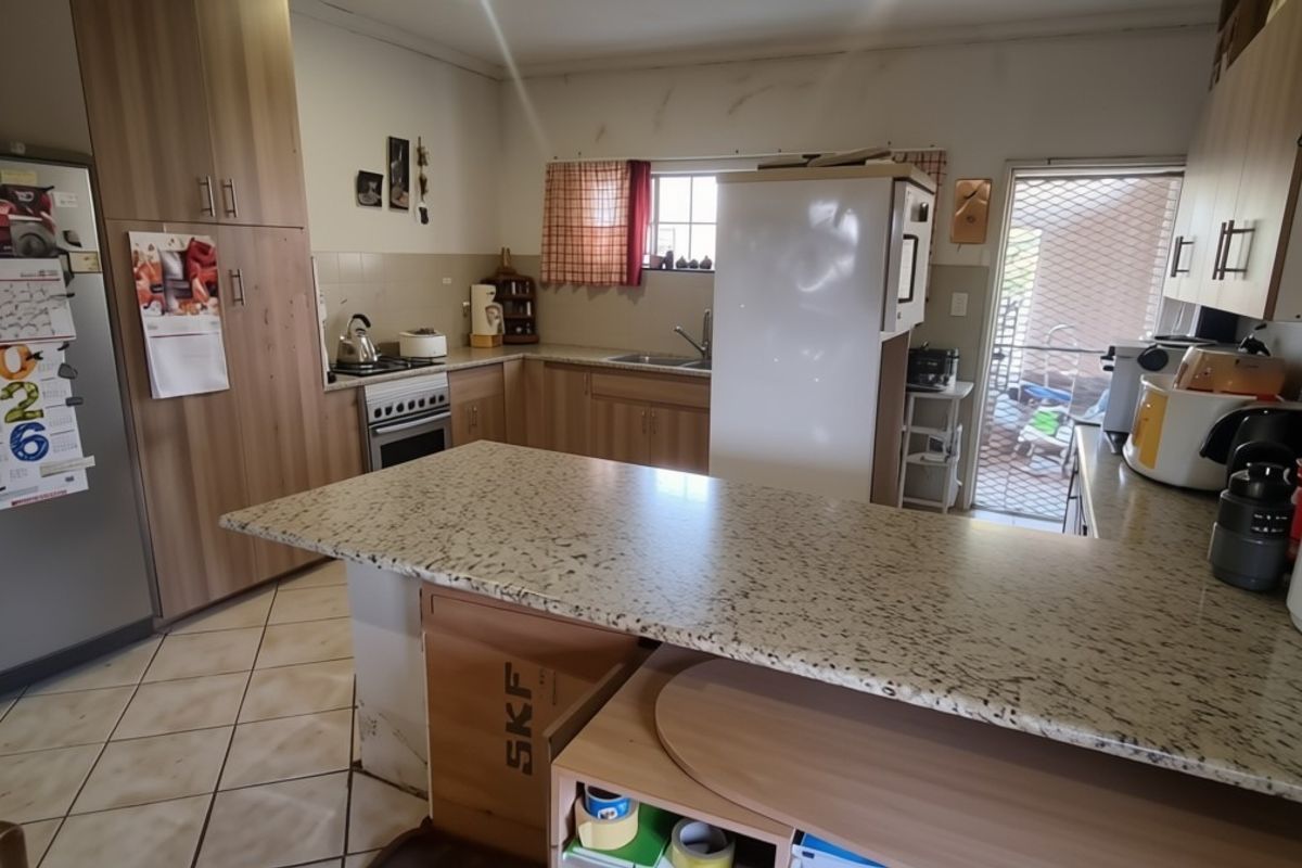 Functional kitchen featuring laminate cabinetry, granite-look countertops, built-in oven and hob, and ceramic floor tiles with direct access to an outdoor area.