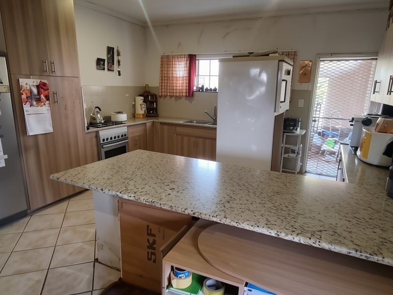 Functional kitchen featuring laminate cabinetry, granite-look countertops, built-in oven and hob, and ceramic floor tiles with direct access to an outdoor area.