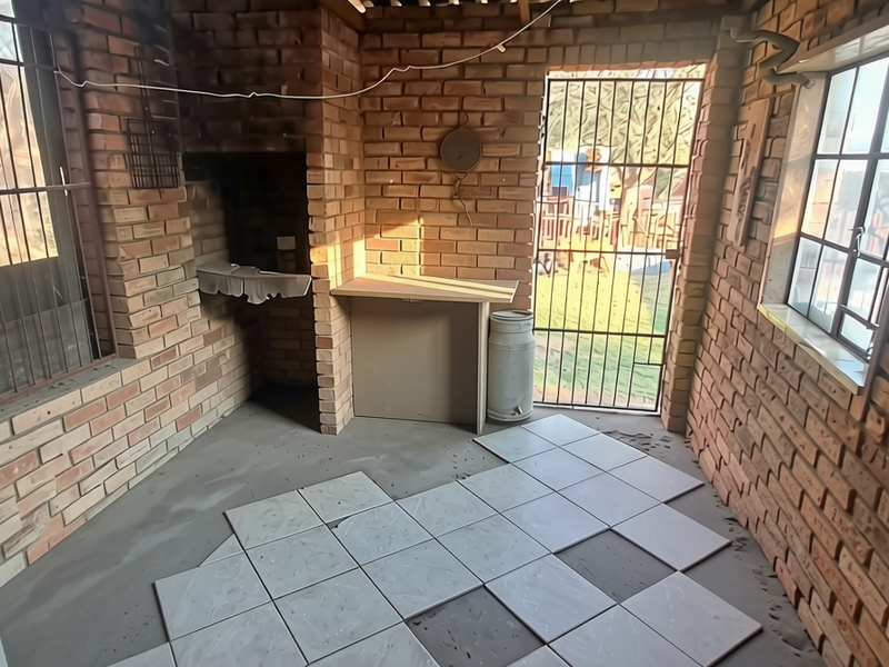 Covered patio area featuring exposed brick walls, a built-in braai, and partially installed floor tiles, offering potential for a functional outdoor entertainment space.
