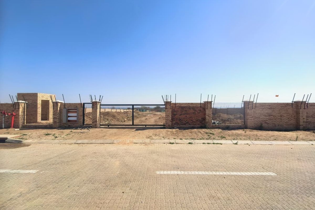 Front view of a vacant commercial plot featuring a brick boundary wall, electric fencing, and a secure metal sliding gate access point.