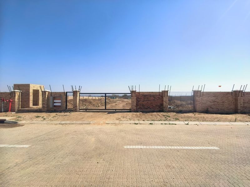 Front view of a vacant commercial plot featuring a brick boundary wall, electric fencing, and a secure metal sliding gate access point.
