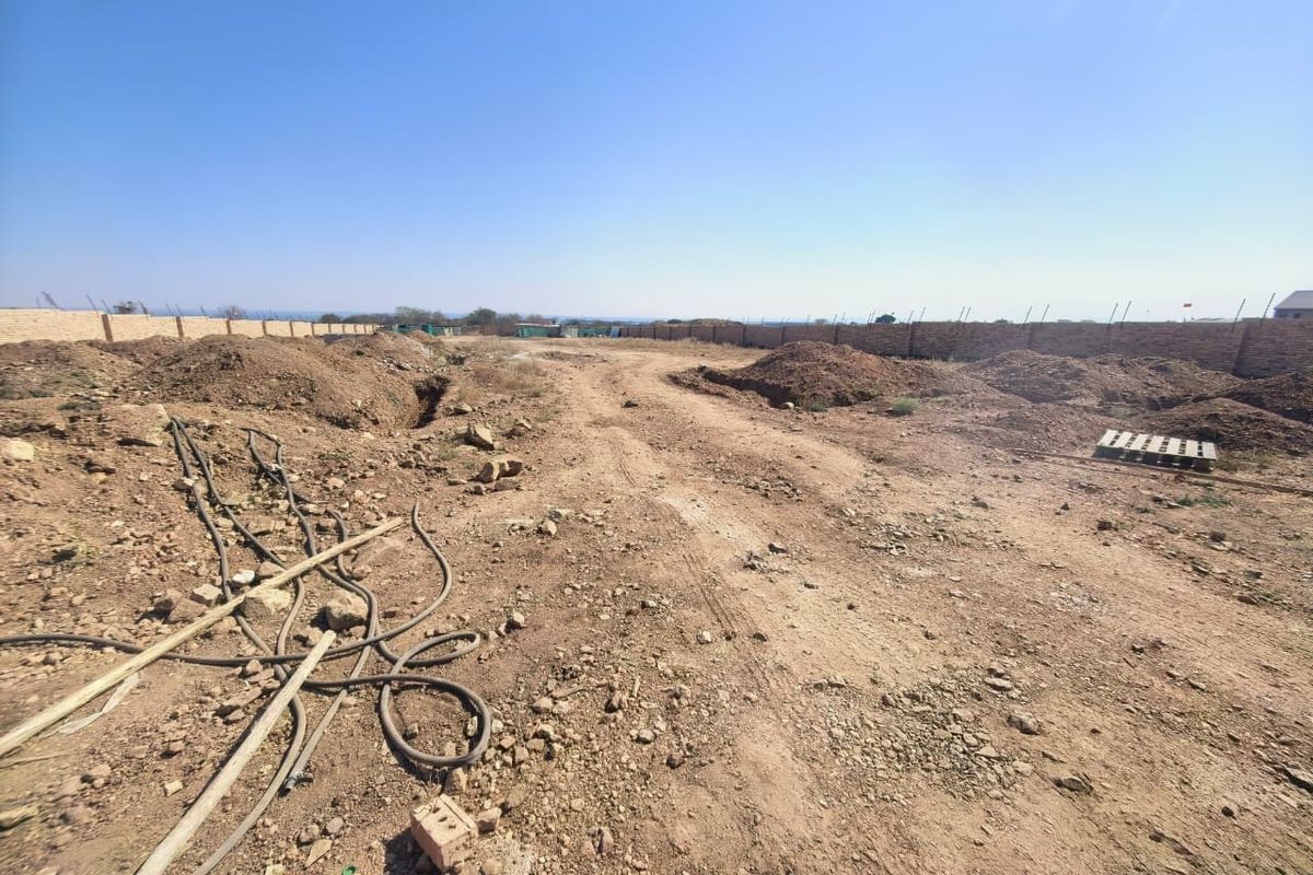 A view of a vacant commercial land plot featuring an enclosed perimeter brick wall and unpaved, uneven ground.
