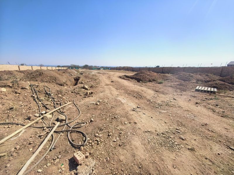 A view of a vacant commercial land plot featuring an enclosed perimeter brick wall and unpaved, uneven ground.