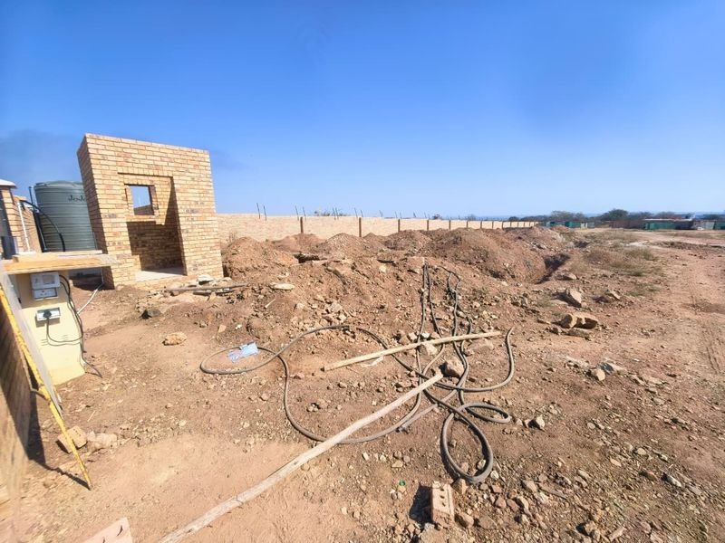 Vacant commercial land featuring a brick boundary wall, a small brick utility structure, and a water storage tank on site.