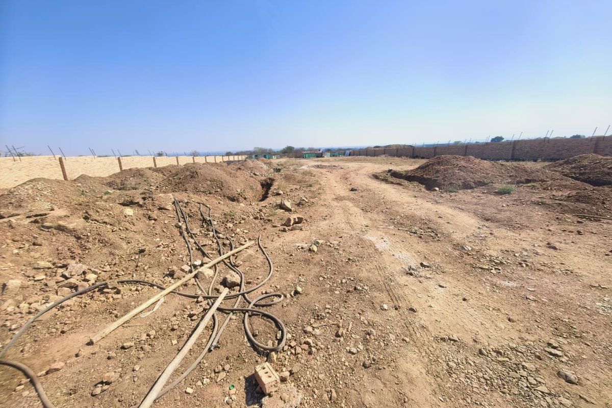 A wide-angle view of a vacant commercial plot featuring perimeter brick walling and unpaved ground with visible site debris.