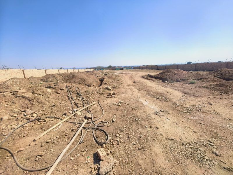 A wide-angle view of a vacant commercial plot featuring perimeter brick walling and unpaved ground with visible site debris.
