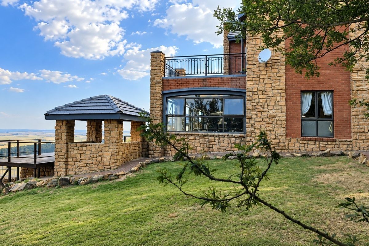 Rear view of the lodge featuring stone and brick exterior, a raised wooden deck, and a stone gazebo overlooking the landscape.