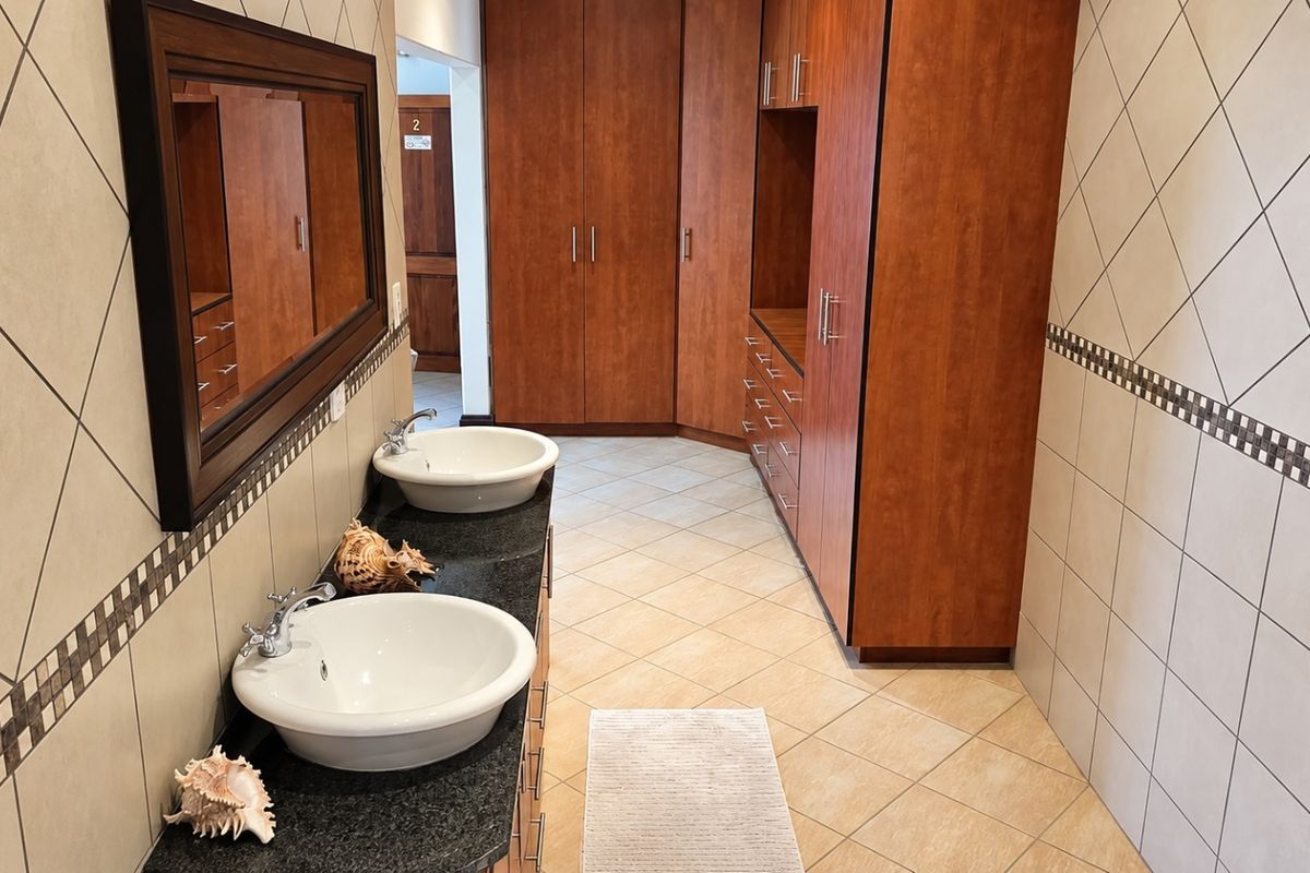 A spacious bathroom featuring a double vanity with vessel sinks, granite countertops, extensive built-in wooden cabinetry, and neutral ceramic tiling throughout.