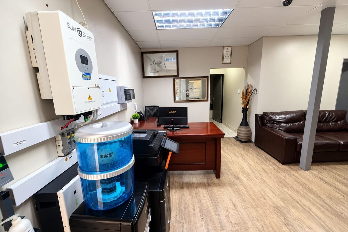 A functional office space featuring a wall-mounted solar inverter, electrical distribution board, security camera, and durable laminate flooring.