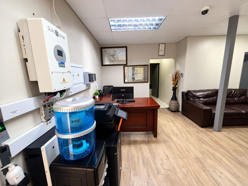 A functional office space featuring a wall-mounted solar inverter, electrical distribution board, security camera, and durable laminate flooring.