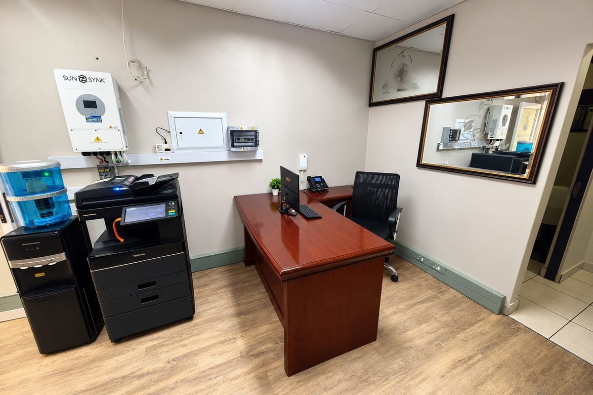 A functional office space featuring a suspended ceiling, integrated inverter system, and wall-mounted electrical distribution board with wood-look flooring.